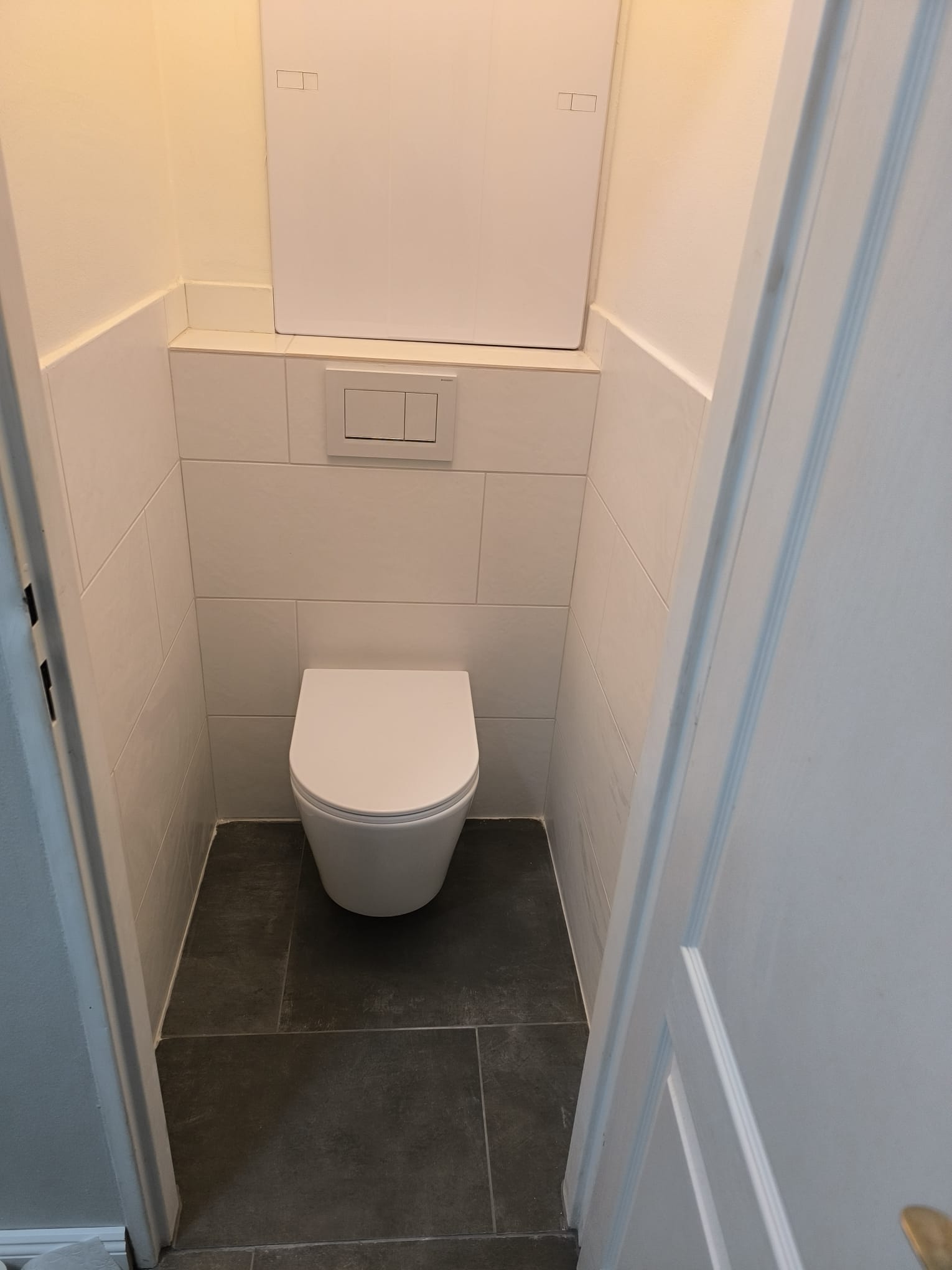 Hotové závěsné WC po rekonstrukci se světlým obkladem a tmavou dlažbou