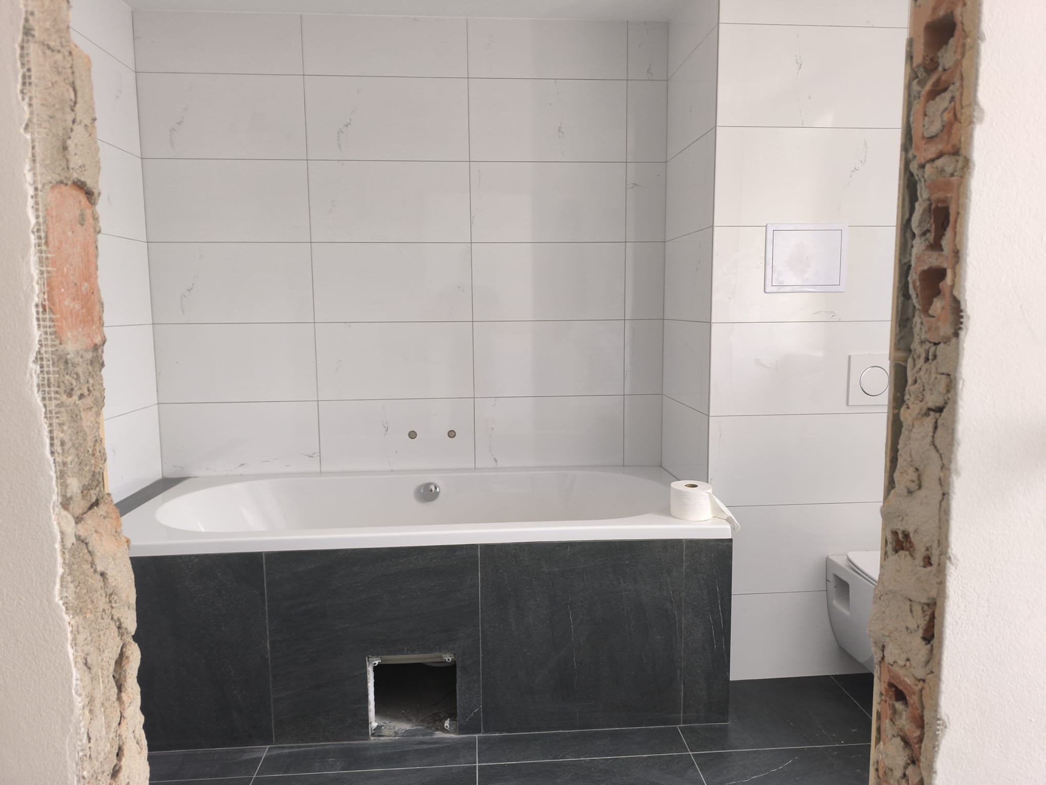 Hotová koupelna s vanou, světlými obklady a tmavou dlažbou po rekonstrukci